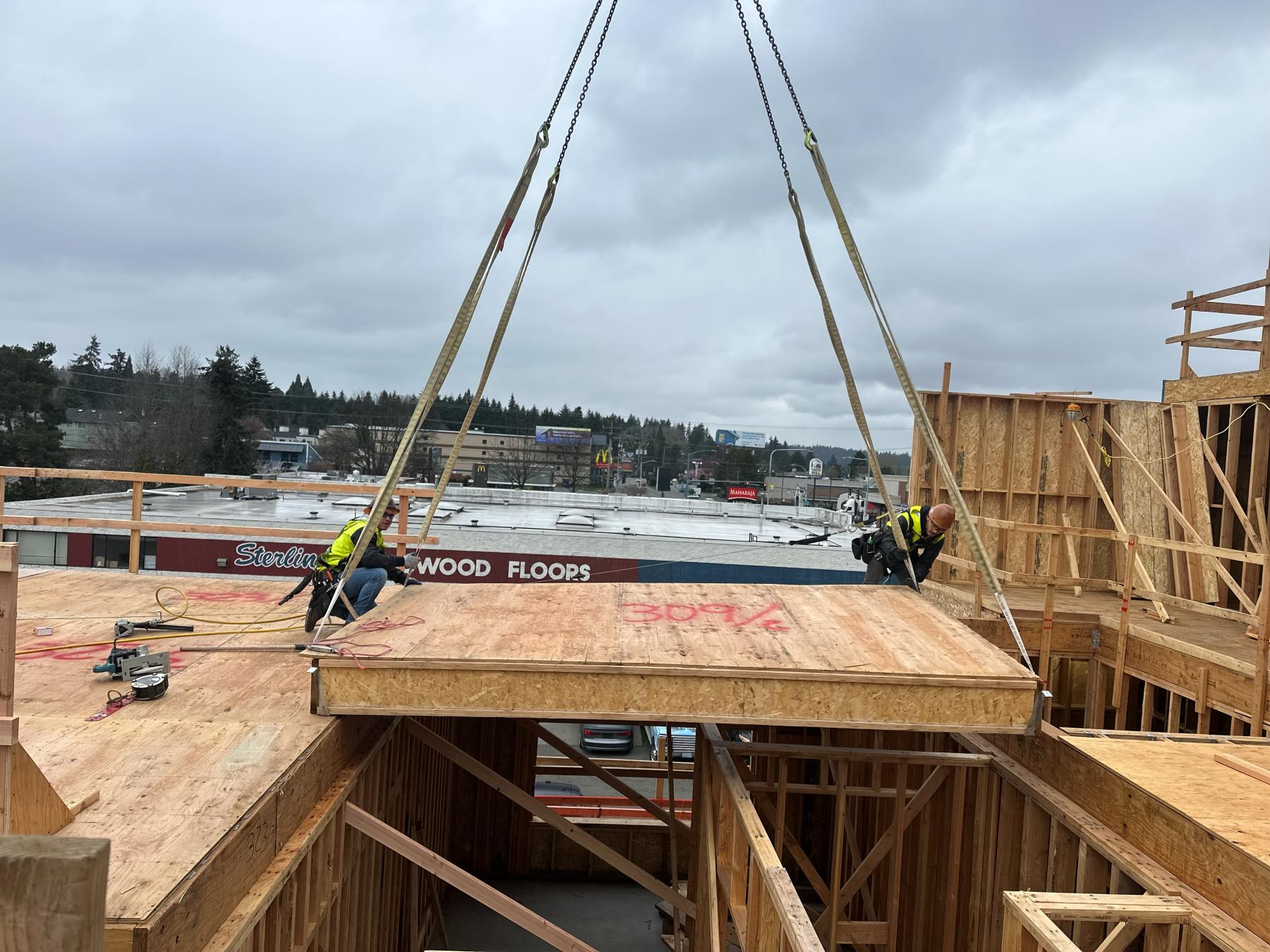TBG framing crew guiding a crane-set floor panel into place on an urban multifamily project in the Seattle area
