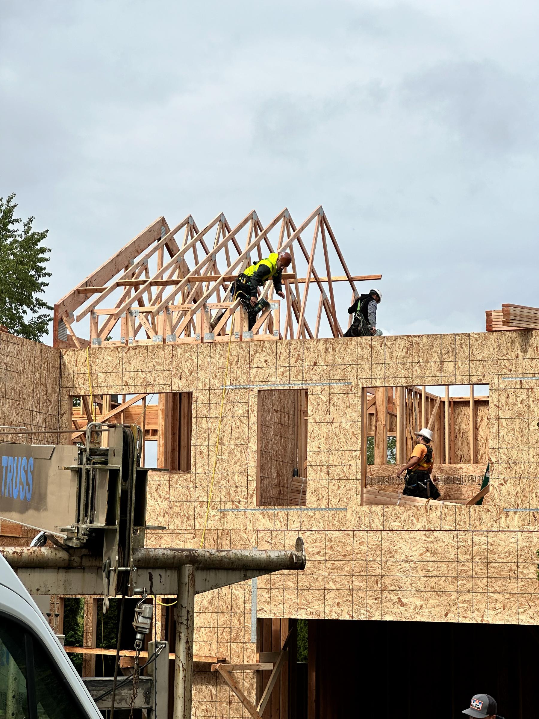 TBG framers setting roof trusses on a two-story building, crew working at height with truss crane below