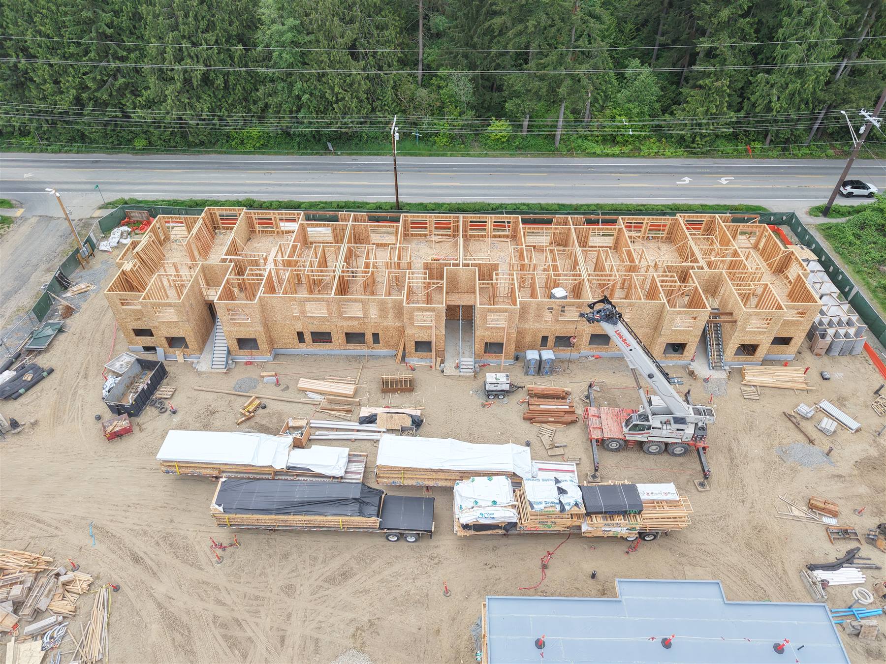 Row of townhomes fully framed with boom truck delivering lumber, aerial view