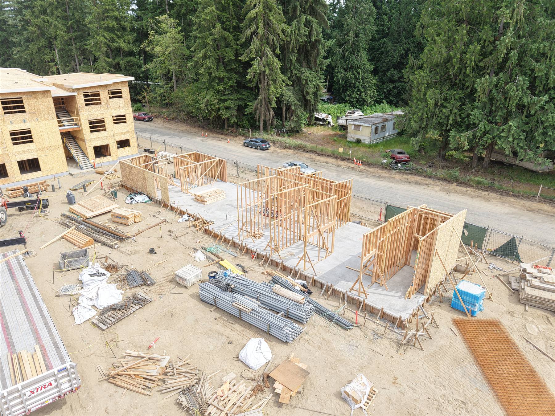 First-floor wall framing standing on slab with a completed framed building behind